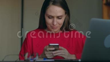穿红色运动衫的女学生在家里的工作场所使用智能手机。
